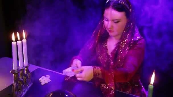 Eine junge Zigeunerin mit Kerzen im Rauch führt die Karten über die Spiegelkugel — Stockvideo