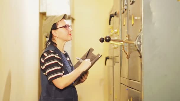Una ingeniera eléctrica femenina registra las lecturas de los aparatos eléctricos en la centralita — Vídeo de stock