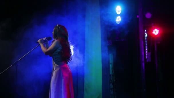 Молода червоноволоса співачка співає на сцені з професійним освітленням і пуфиками диму. Стрілянина . — стокове відео