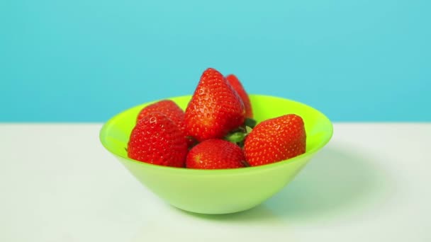 Bayas fresas rojas maduras en un tazón verde sobre un fondo azul . — Vídeos de Stock