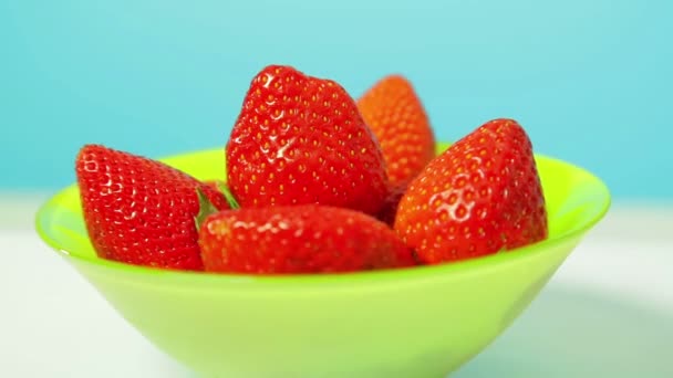 Rode bessen sappige aardbeien in een groene kom op een blauwe achtergrond draait in een cirkel — Stockvideo