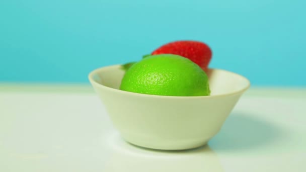 Ασβέστη πράσινο φρούτων και ώριμη φράουλα μούρο σε μια λευκή πλάκα περιστρέφεται σε έναν κύκλο. — Αρχείο Βίντεο