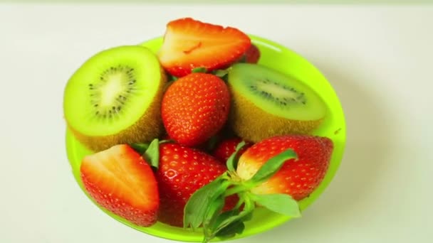 Fresh kiwi and sliced strawberries on a blue background on a plate rotates in a circle. View from above — Stock Video