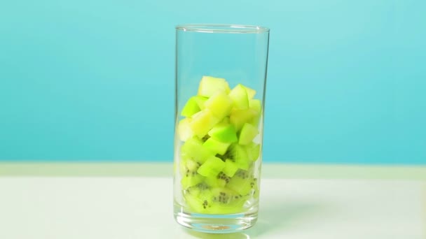 У прозорому склі нарізані скибочки фруктів ківі та яблука. Скло обертається в колі . — стокове відео