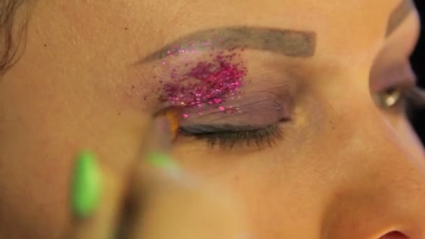 Die weibliche Hand mit einem Pinsel trägt helle lila Funken auf die Augenlider auf — Stockvideo