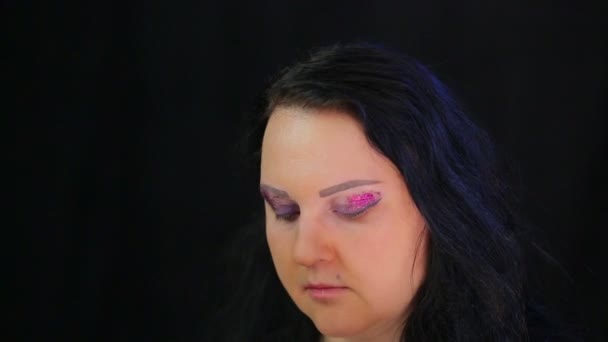 En brunett kvinna applicerar ljusa skuggor och lila gnistrar till hennes ögonlock. Tid varv. — Stockvideo