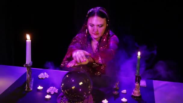 В волшебном салоне цыганка читает будущее в волшебном шаре, окруженном сиянием и дымом. — стоковое видео