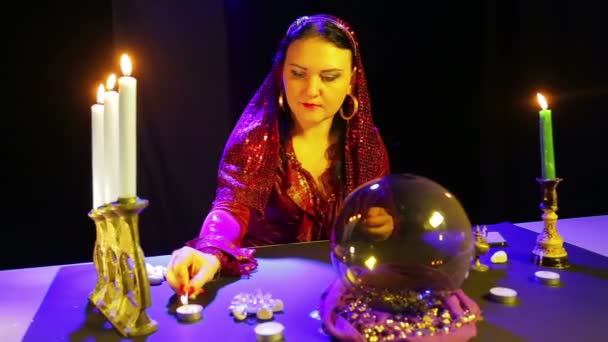 A gypsy woman in a red dress in a divination room lights candles on a table — Stock Video