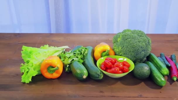 På trä bordet är färska grönsaker zucchini, broccoli, sallad, avokado, gurkor, peppar och chilipeppar, körsbärs tomater. — Stockvideo