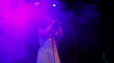 Genç bir kızıl saçlı şarkıcı, profesyonel aydınlatma ve duman Puffs ile sahnede şarkı söylüyor. Ortalama plan