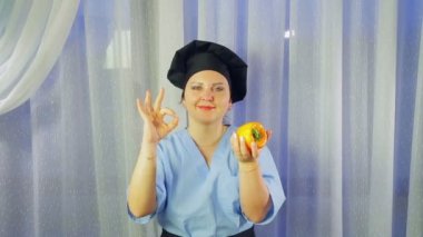 Bir kadın önlük gülümsüyor aşçı, elinde sarı bir biber tutar ve elini ile ok gösterir. Ortalama plan