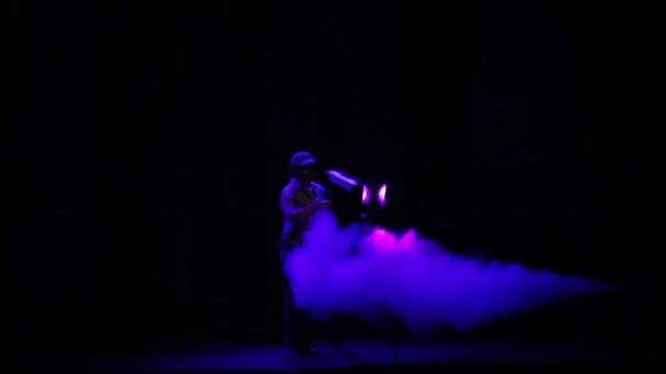Oświetlacz kobiety kieruje wiązką światła z reflektora do hali w Puff dymu. — Wideo stockowe