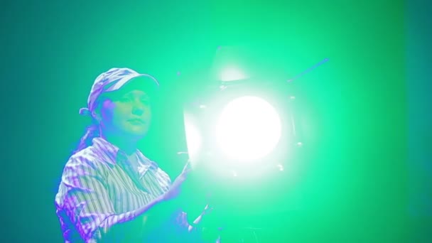 Una joven iluminadora en escena dirige el haz de un proyector de perfil — Vídeo de stock