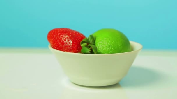 Lime fruit and ripe strawberries on a white plate rotates in a circle — Stock Video