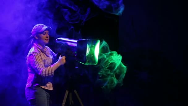 Una joven iluminadora en el escenario trabajando con un proyector de perfil teatral induce la luz en las nubes de humo . — Vídeos de Stock