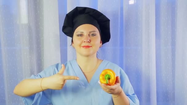 A female cook smiles, holds a yellow pepper in her hand and points to it — Stock Video