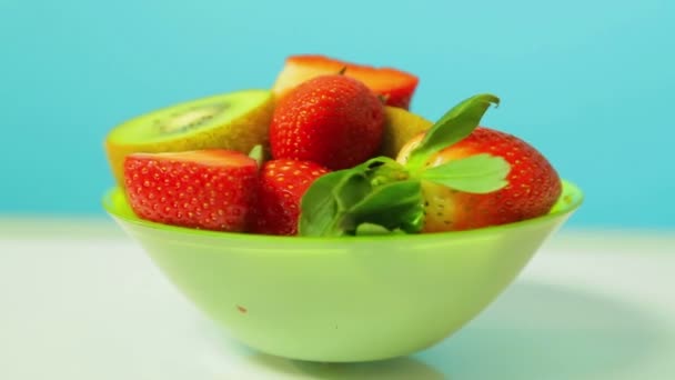 Färska Kiwi och skivade jordgubbar på en blå bakgrund på en grön tallrik roterar i en cirkel — Stockvideo