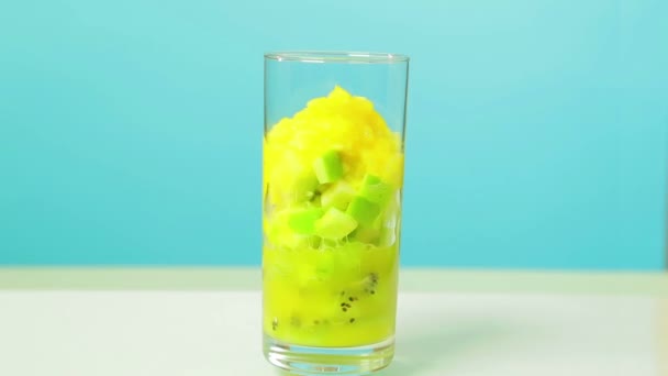 In einem Glas werden Kiwi-Scheiben und ein Apfel geschnitten und Orangensaft ausgeschenkt. Glas dreht sich im Kreis — Stockvideo