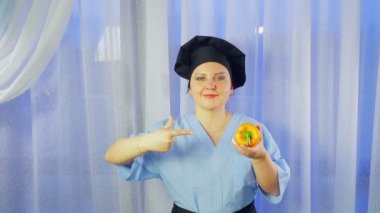 Bir kadın aşçı gülümsüyor, elinde sarı bir biber tutar ve ona işaret.