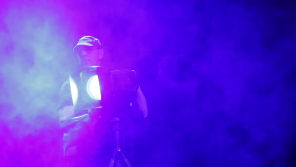 Ένας άντρας Φωτιστής κατευθύνει μια ακτίνα φωτός στο προσκήνιο από τη σκηνή στην αίθουσα σε μια ριπή καπνού — Αρχείο Βίντεο