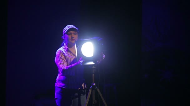 Una joven iluminadora en el escenario trabajando con un proyector de perfil teatral induce la luz en las nubes de humo — Vídeo de stock