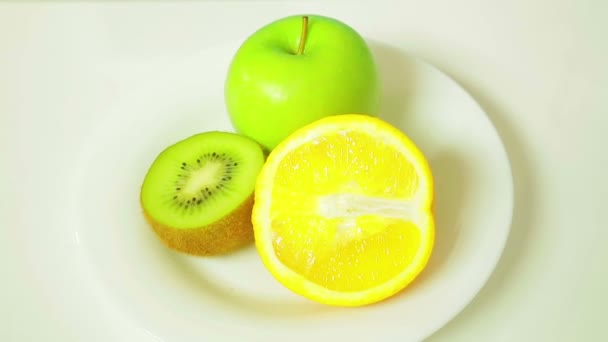 Половинки оранжевого киви и зеленого яблока на белой тарелке вращаются по кругу — стоковое видео