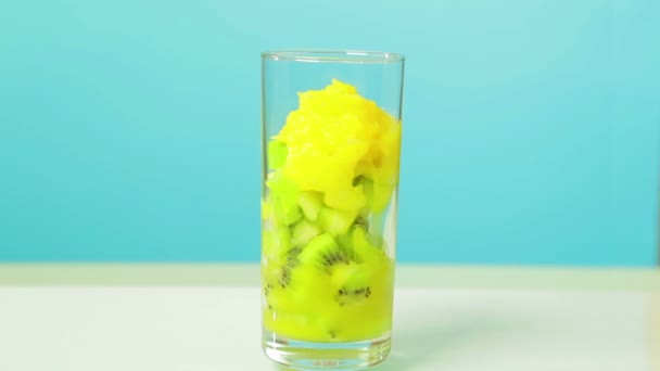 In een glas schijfjes Kiwi fruit en een appel worden gesneden en jus d'orange gegoten. Glas draait in een cirkel — Stockvideo