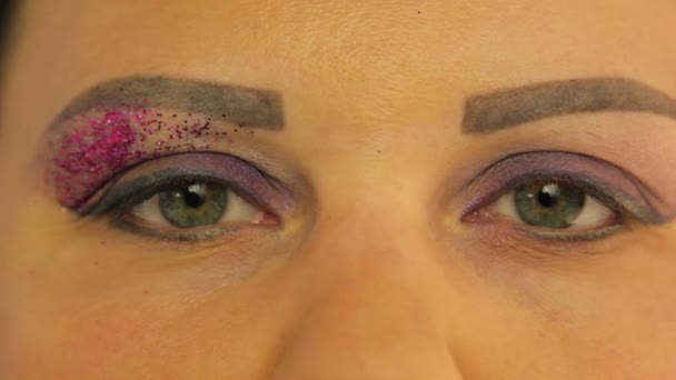 Kvinnliga ögon med en lila make-up på ena ögat ljusa lila gnistrar — Stockvideo