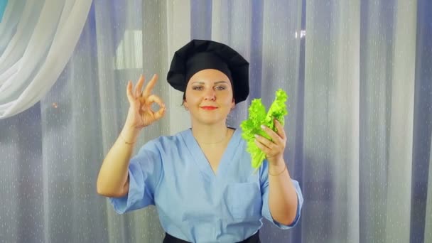 Woman cook in apron smiles, holds green salad in hand and shows hand OK — 비디오