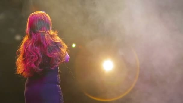 Den rödhåriga skådespelerskan i en lysande svart klänning sjunger priset på en puff av rök. Skytte från bak — Stockvideo