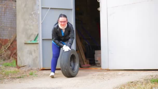 Женщина выкатывает автомобильное колесо с диском из гаража — стоковое видео