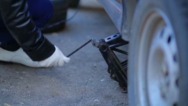 Mujer en guantes levanta el coche con un gato — Vídeo de stock