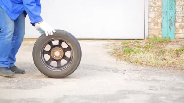En man rullar en bildäck med en skiva på asfalt. — Stockvideo