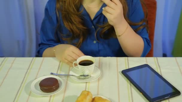Žena v kavárně u stolu, pije kávu s dezertem a čte si novinky na tabletu — Stock video