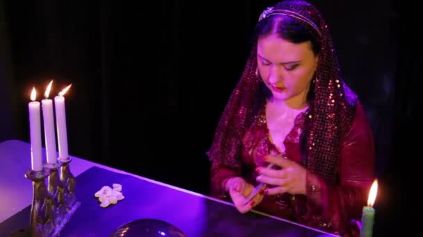 Um jovem cigano à luz de velas nos destaques embaralha o cartão — Vídeo de Stock