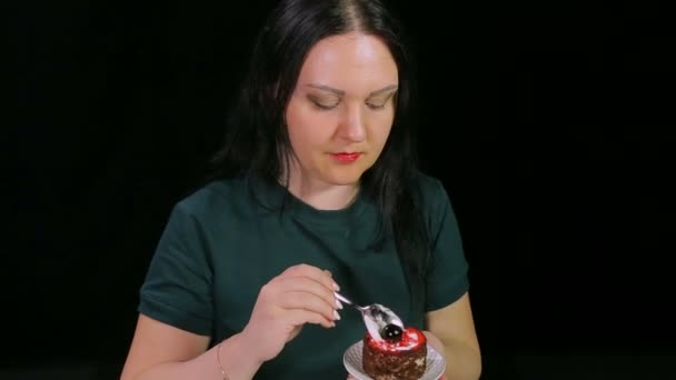 Uma mulher morena em um fundo preto está bebendo café e comendo um bolo — Vídeo de Stock