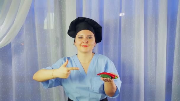 Donna cuoco in grembiule sorride, tiene peperoncini in mano e indica loro — Video Stock