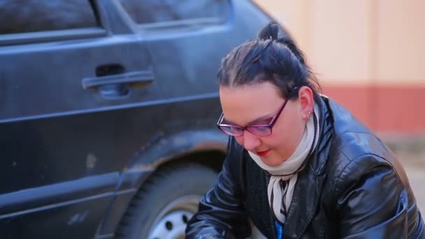 Eine Frau mit Brille schraubt den Stecker am Autoreifen auf der Scheibe ab — Stockvideo