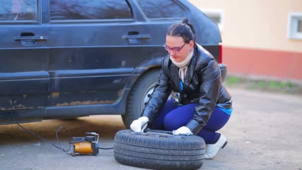 Жінка в рукавичках накачує автомобільну шину компресором — стокове відео