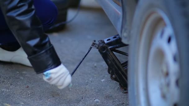 Mujer en guantes levanta el coche con un gato . — Vídeos de Stock