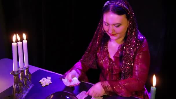 En leende zigenare i den magiska salongen med levande ljus läser framtiden på korten — Stockvideo