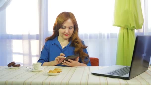 テーブルのカフェで茶色の髪の女性がタブレットで作業し、コーヒーを飲む. — ストック動画