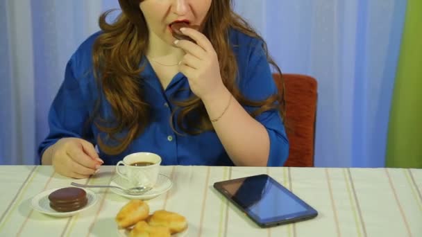 Γυναίκα σε ένα καφέ σε ένα τραπέζι πίνοντας καφέ με επιδόρπιο και διαβάζοντας τα νέα στο tablet — Αρχείο Βίντεο