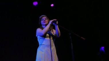 Genç bir kızıl saçlı şarkıcı sahnede bir mikrofon ile konser veren şarkı söylüyor. Çekim tarafı