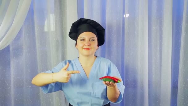 Mujer cocinera en delantal sonríe, sostiene chiles en su mano y señala a ellos — Vídeo de stock