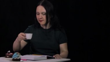 Kafede bir kadın siyah bir arka plan üzerinde beyaz bir fincan kahve içiyor ve bir günlük yazıyor