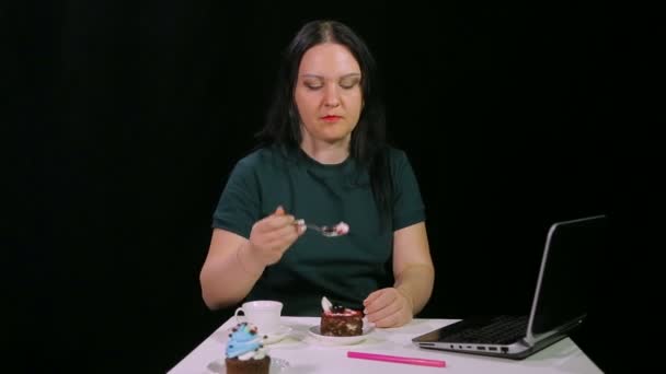 Une femme brune sur fond noir dans un café boit du café et mange un gâteau — Video