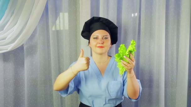 Perempuan memasak dengan senyuman apron, memegang salad hijau di tangan dan menunjukkan kelas dengan tangan . — Stok Video