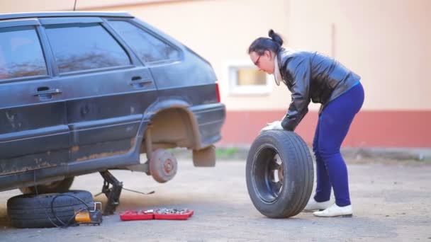 Eine Frau in Handschuhen legt einen Reifen auf eine Scheibe an der Achse eines Autos — Stockvideo