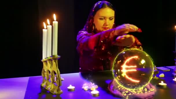 Una mujer gitana en un salón mágico está adivinando sobre una bola de cristal y un signo de euro aparece en ella — Vídeo de stock